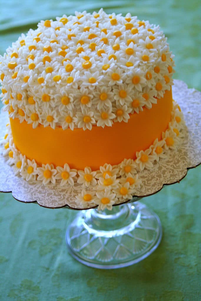 a lemon cake decorated with white frosting and tiny white and yellow fondant daisies