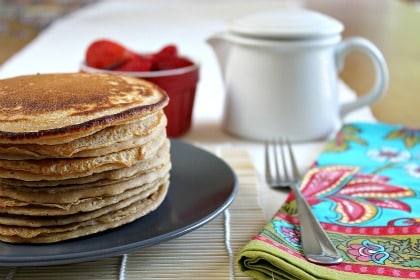 A stack of pancakes on a plate with syrup and fresh fruit.