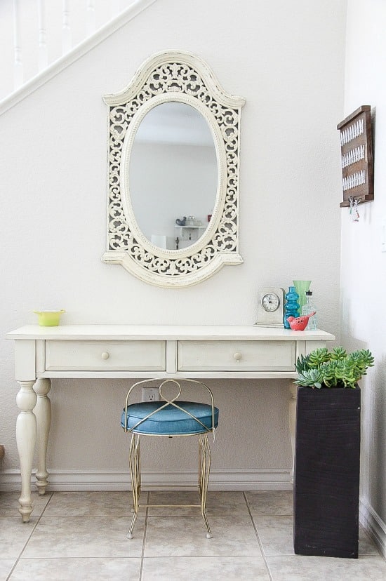 entryway of a home with a bench, mirror, stool, umbrella stand planter, and decor.