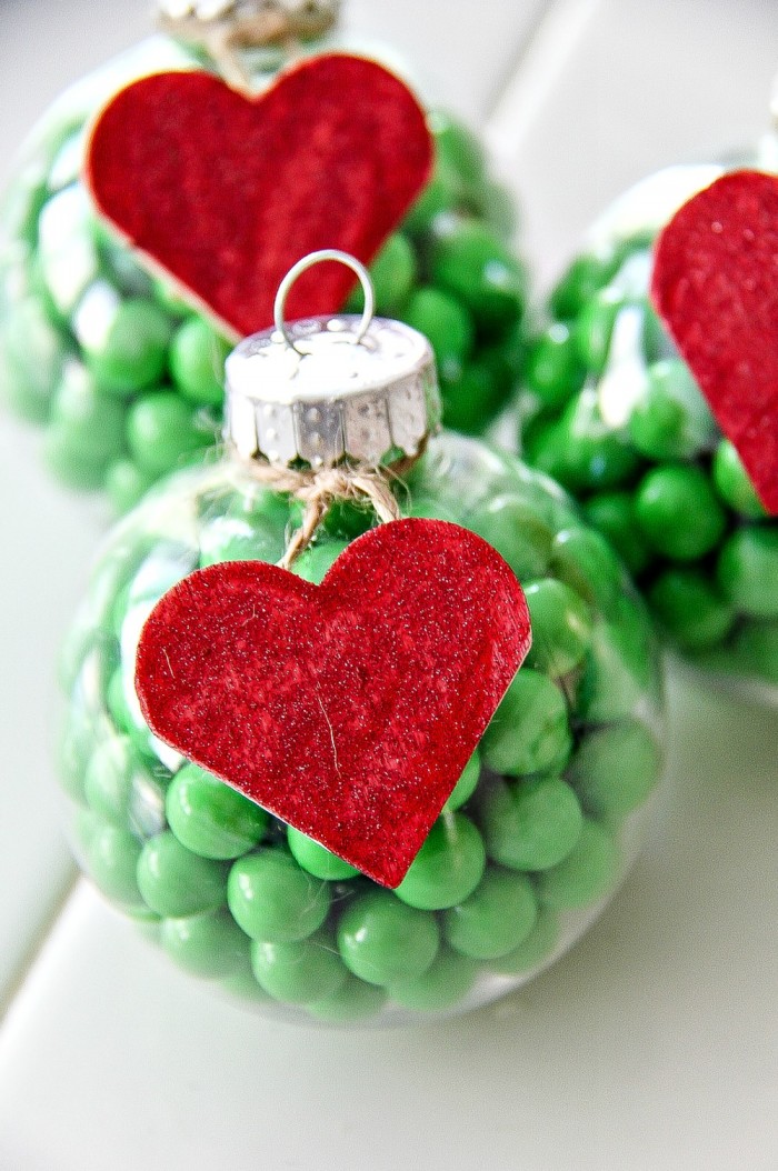 clear christmas ornaments filled with green candy and a red wood heart on the outside