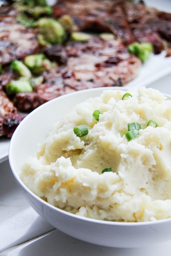 mashed potatoes with green onions in a white bowl with pork chops in the background