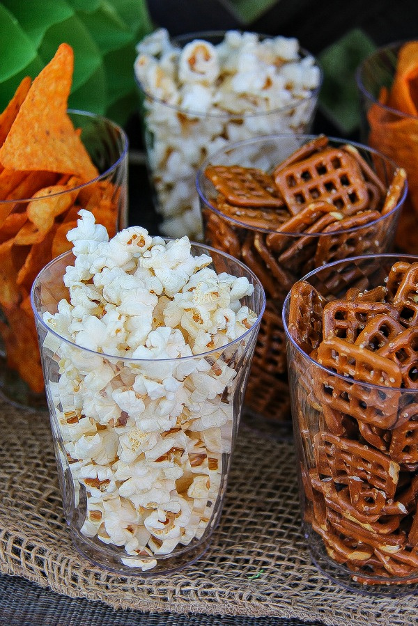 clear drinking cups filled with popcorn, pretzels, and corn chips