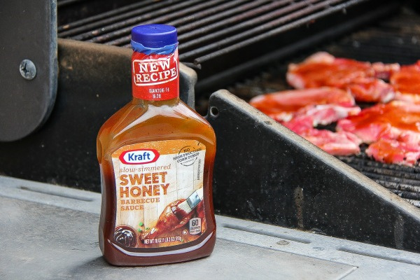 a bottle of kraft sweet honey barbecue sauce next to a grill with pork chops cooking