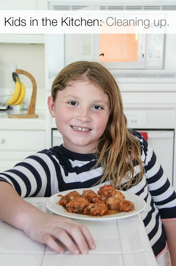 a girl standing at a kitchen counter with hot wings on a plate