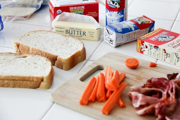 bread, carrot sticks, and bacon on a counter to make lunch