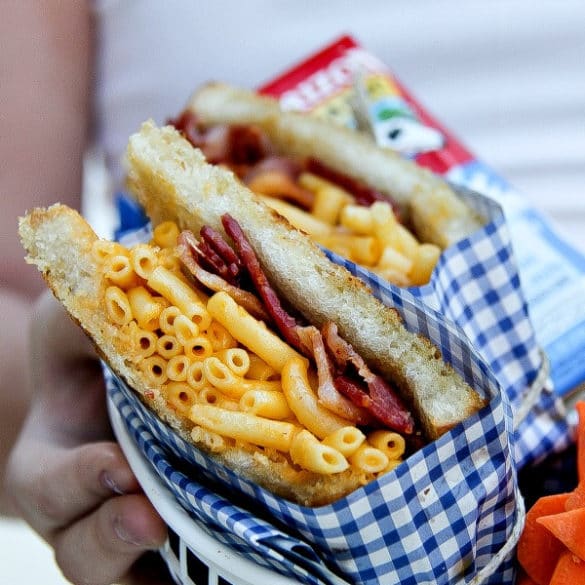 girl holding a food basket containing a bacon with mac & cheese sandwich