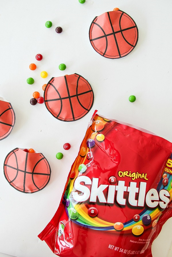 a bag of skittles with paper basketballs scattered