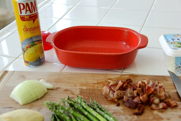 a small orange casserole dish with bacon, asparagus, and onion
