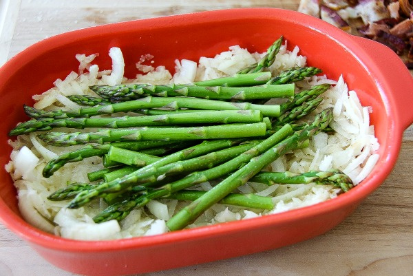 hash browns in the bottom of a casserole dish with asparagus on top