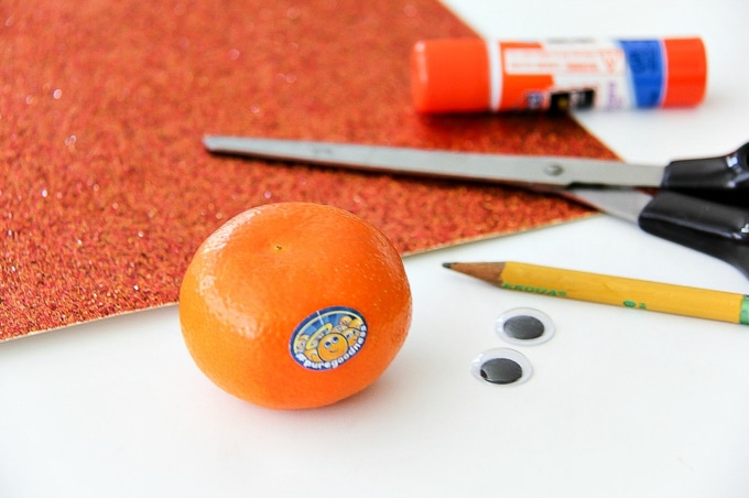a mandarin, orange glitter card stock, googly eyes, scissors, and glue to make a fun snack with fruit.