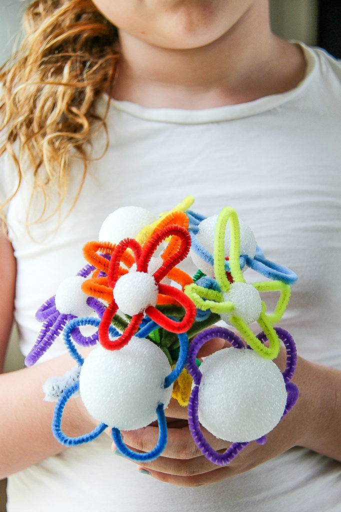 girl holding flowers made out of pipecleaners and foam balls