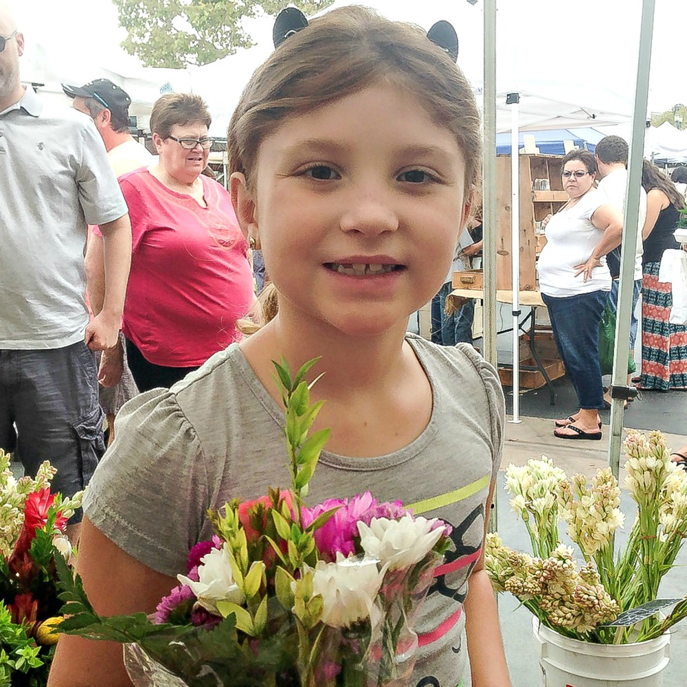 a girl buying flowers at a farmers market