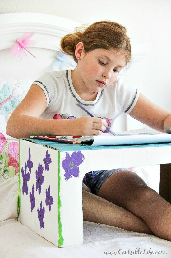 a lap tray made out of a cardboard box with a girl working on it