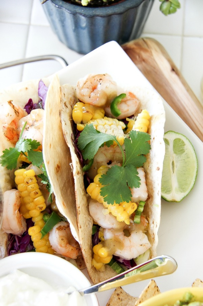 two shrimp and corn tacos on a white plate with lime