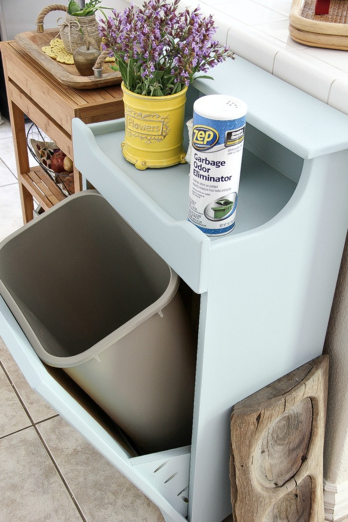 a tilt out wood trash can cabinet open with a plastic trash can inside