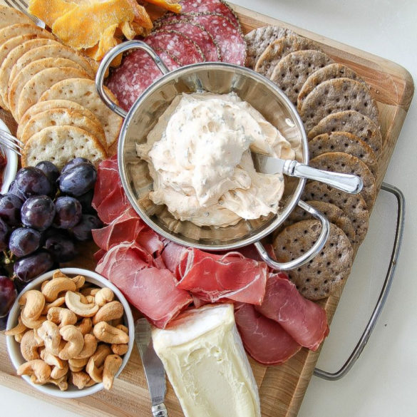 a charcuterie board with nuts, meats, cheese, fruit, and spread