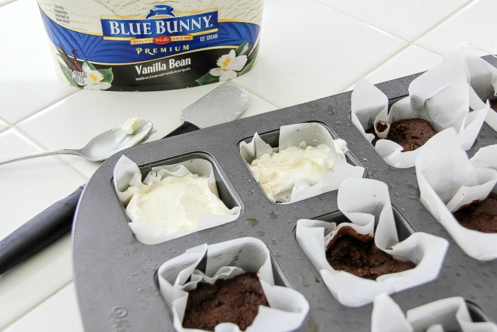 ice cream being put on top of cooked cake in a brownie pan