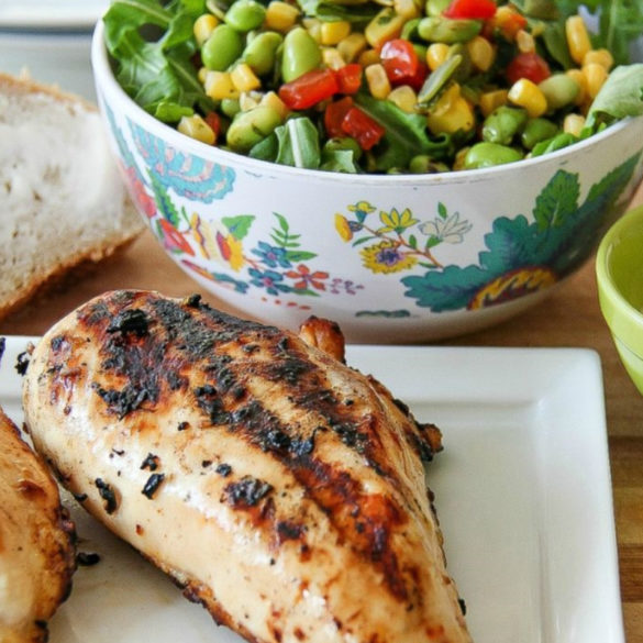 grilled chicken with a bowl of salad behind it