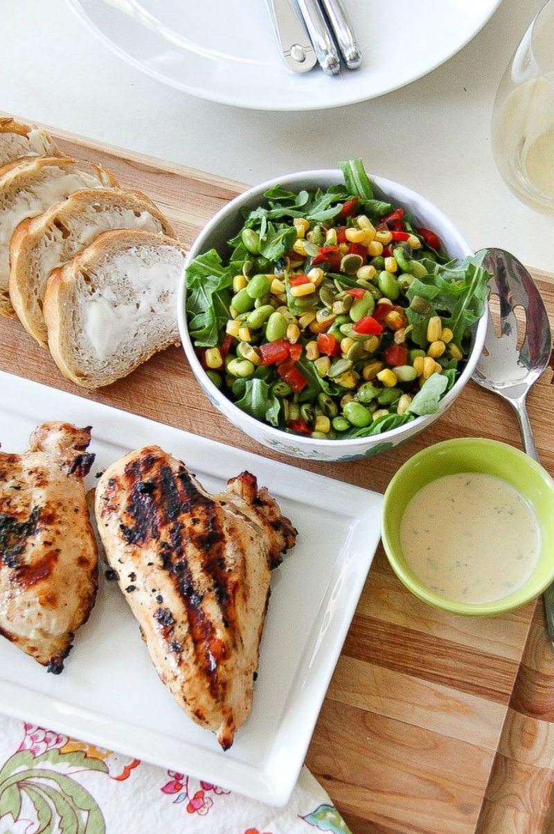 grilled chicken on a serving tray with a side salad and buttered bread