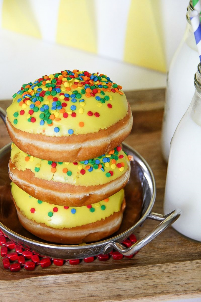 a stack of doughnuts with yellow frosting and colored sprinkles on a silver tray next to milk