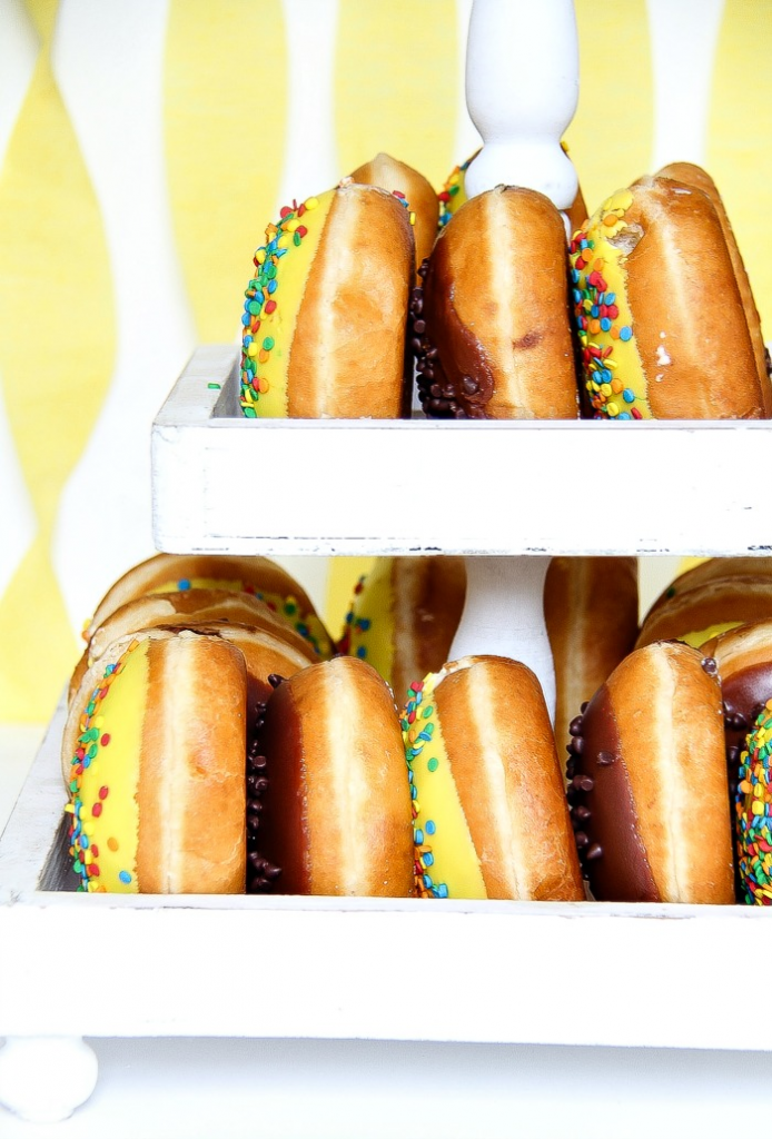 a white wood tiered party food stand filled with assorted donuts