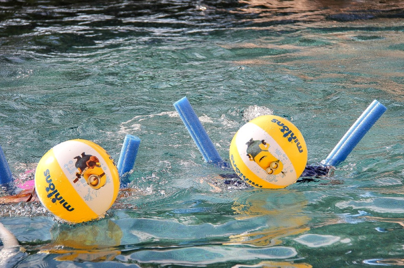 kids in a swimming pool playing with minion beach balls and noodles