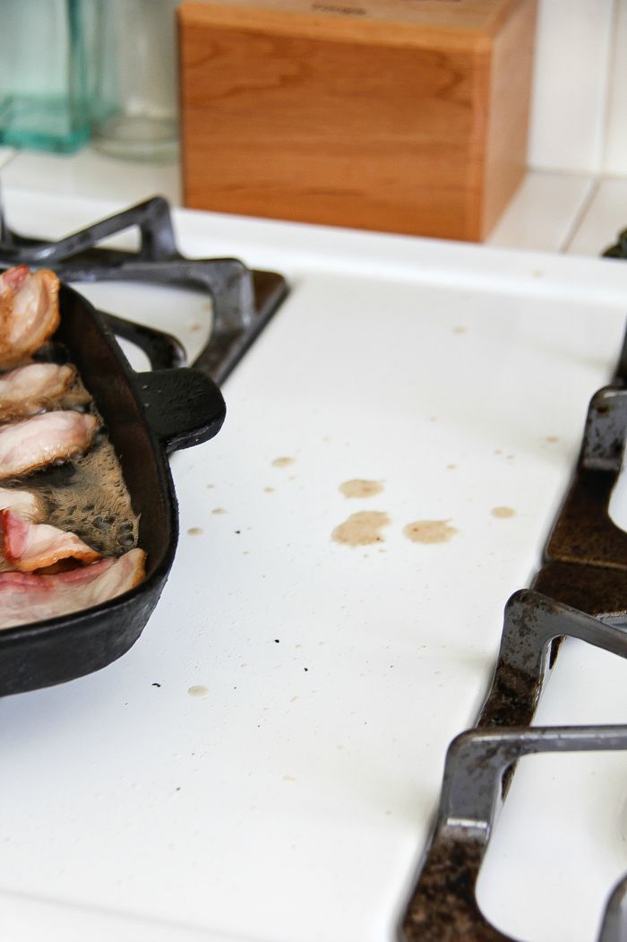 a grill pan with bacon on the stove and grease splattered onto the stove