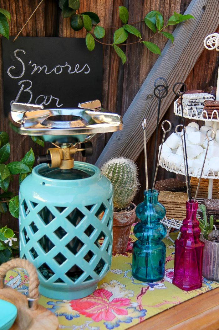 a portable camp stove in a candle holder with colorful jars filled with metal skewers for s'mores