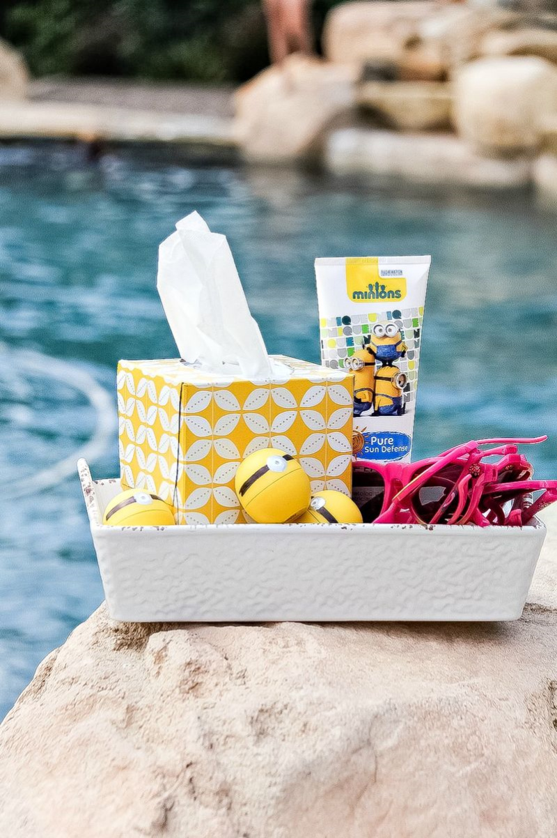 A box filled with minions sunscreen, lip balm, and sunglasses in front of a swimming pool