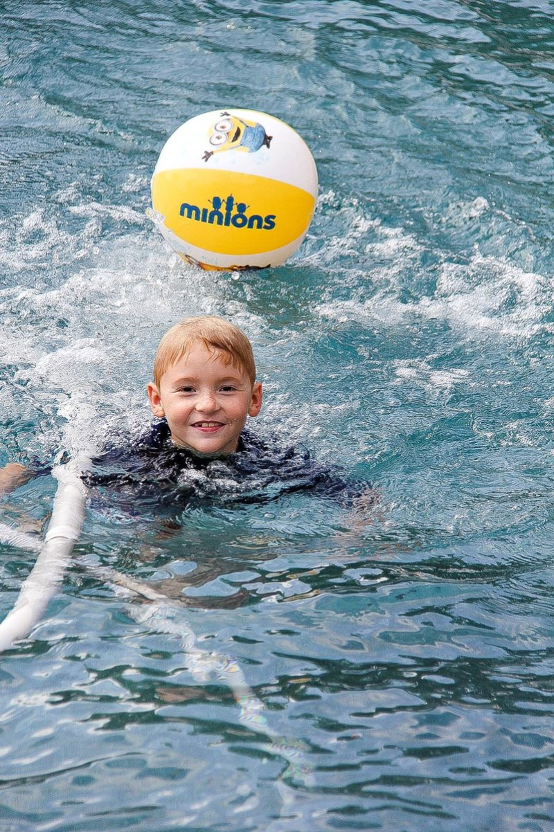 a boy playing in a swimming pool with a minions beach ball