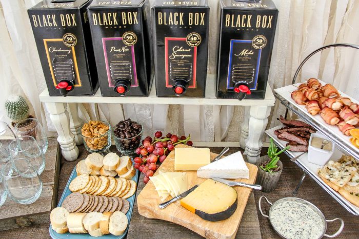 black box wines on a table with assorted cheese, craackers, fruit, and appetizers