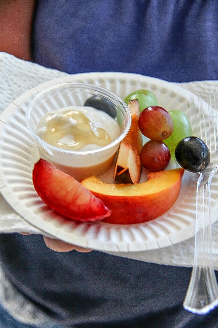 girl holding a paper plate with fresh fruit and yogurt dipping sauce in a container