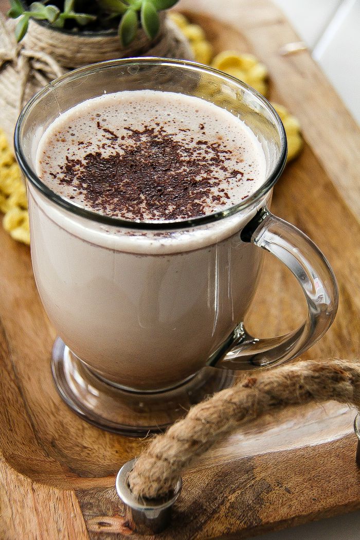 hot chocolate in a clear glass mug on a wood tray