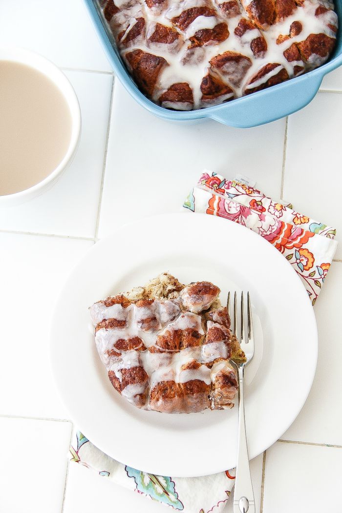 a slice of cinnamon roll casserole on a white plate with coffee and a casserole dish