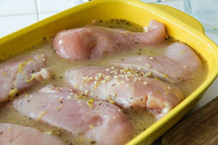 raw chicken in a yellow baking dish covered in lemon marinade