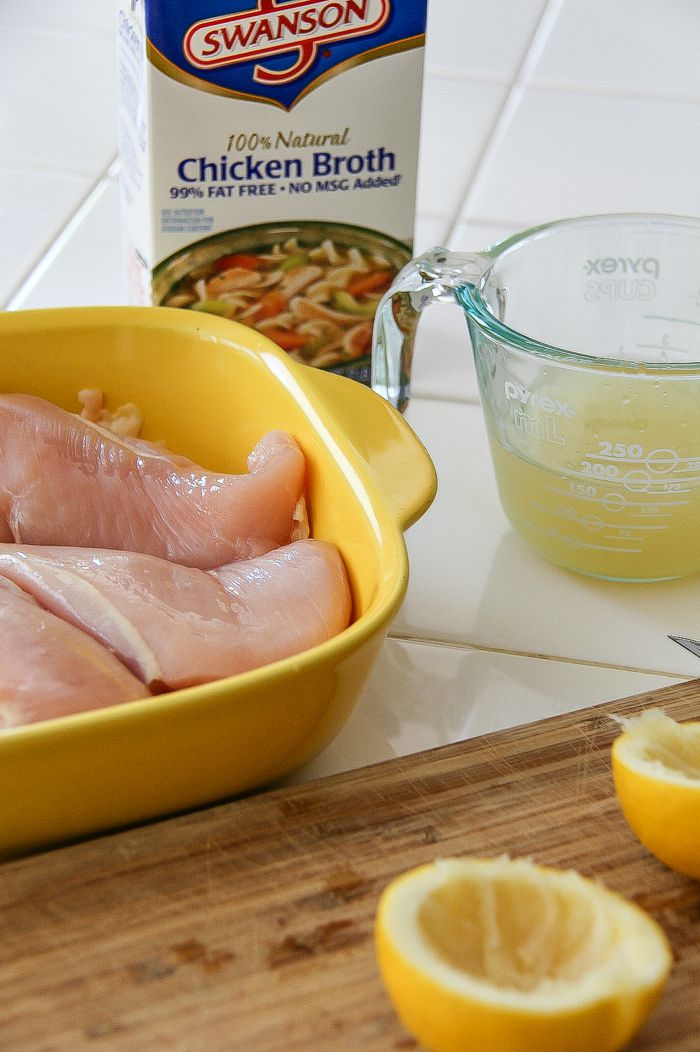 chicken in a dish with broth in a jug and lemon