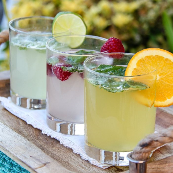 three cocktails garnished with orange, raspberry, and lime