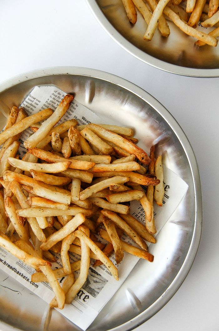 french fries on a silver tray with newspaper print parchment paper