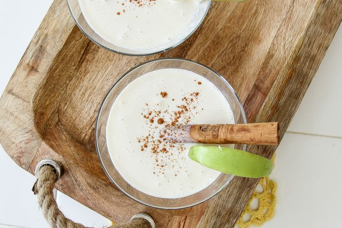 creamy cocktail with apple and a cinnamon stick on a wood tray