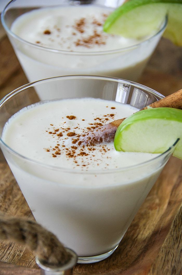 creamy cocktail in a glass with apple and cinnamon stick garnishes