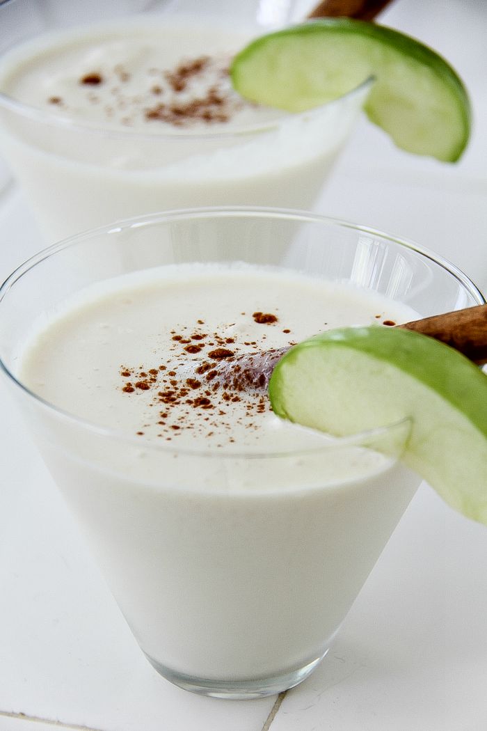 creamy cocktail in a glass with an apple slice and cinnamon stick garnish