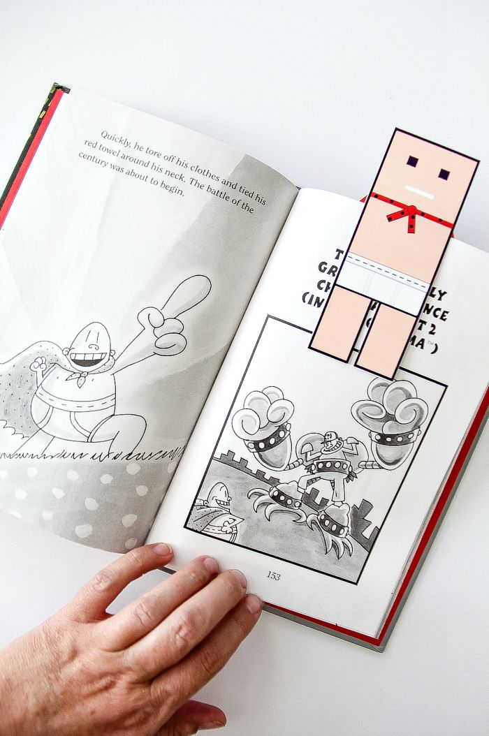 hand holding open a captain underpants book with a paper bookmark