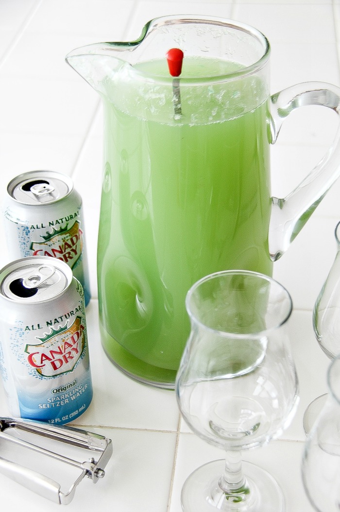 a green drink in a glass jug with glasses and cans of Canada Dry seltzer