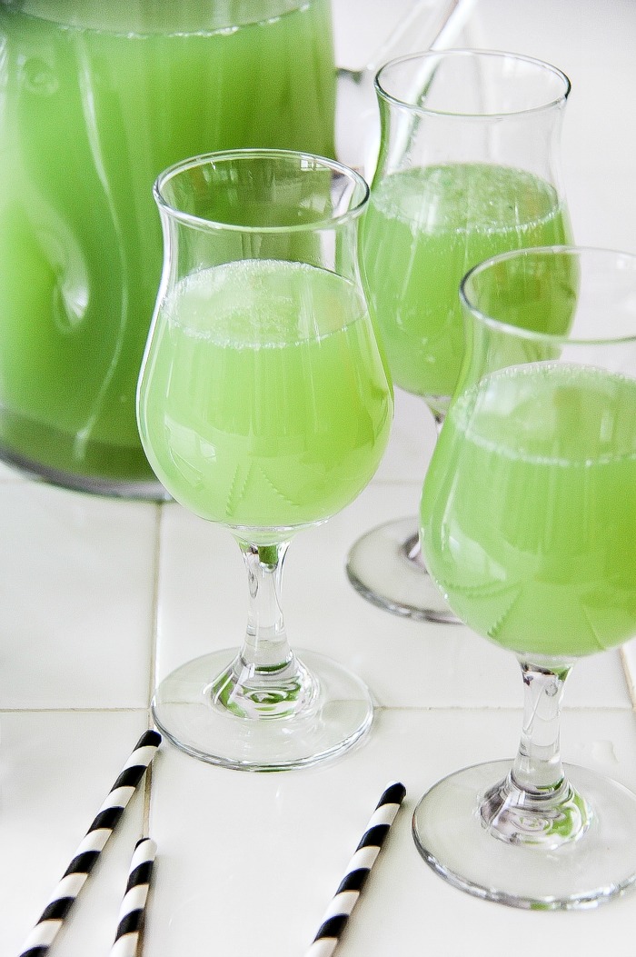 green drinks in cocktail glasses with stems and a glass jug in the background