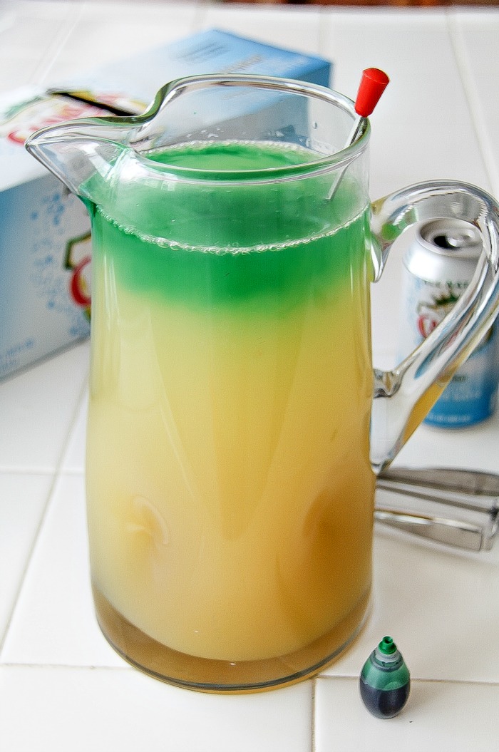 yellow drink in a jug with green food coloring being added