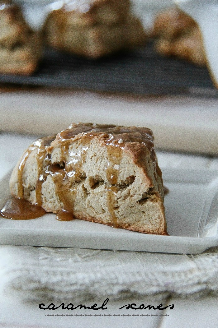 a scone with caramel dripping over the sides and a wire rack of scones in the background