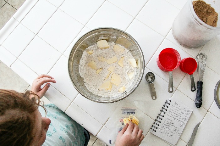 girl in the kitchen adding butter to flour to make scones