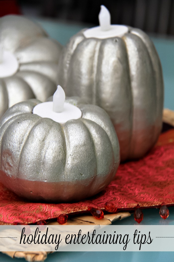 silver painted pumpkins with tea light candles inside them on a red table runner