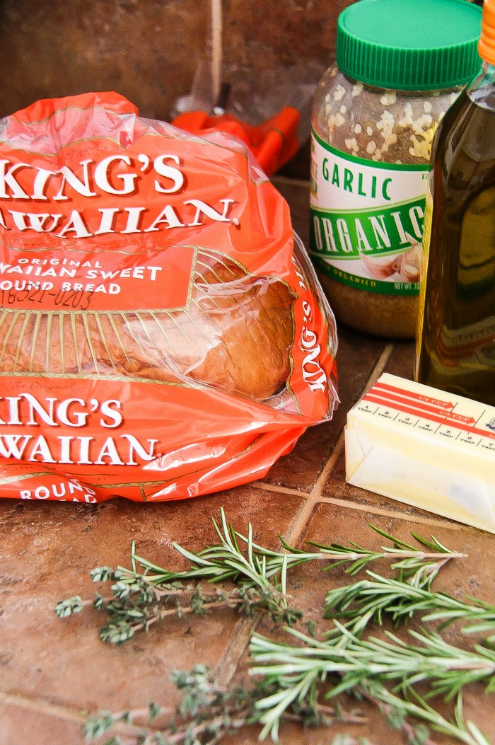 kings hawaiian sweet round bread with a jar of crushed garlic, stick of butter, and fresh rosemary and thyme.