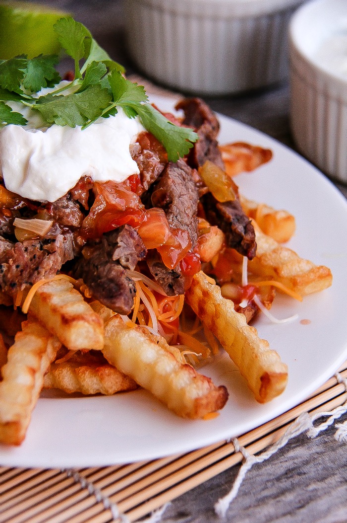 fries topped with carne asada meat, tomatoe, sour cream and cilantro